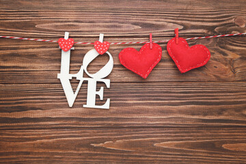 Fabric hearts and word Love hanging on rope on brown wooden background
