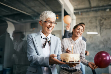 Happy senior businesswoman carries Birthday cake on surprise party in the office.