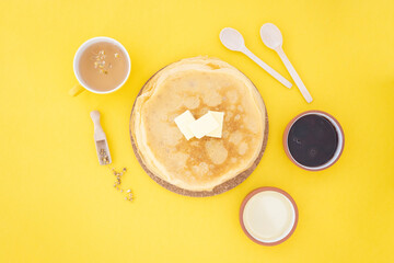Shrovetide Maslenitsa Butter Week festival meal. Russian pancakes with butter, honey and jam on a yellow background. Top view, Flat lay