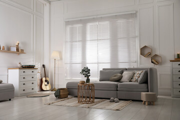 Living room with comfortable grey sofa and stylish interior elements near window