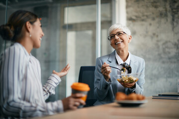Happy senior businesswoman and her younger colleague enjoy a conversation during lunch break in the office.