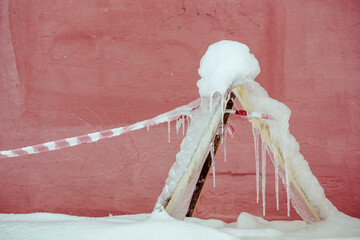 close-up of a wooden triangle and a warning red and white tape near the wall of a house on a snowy street