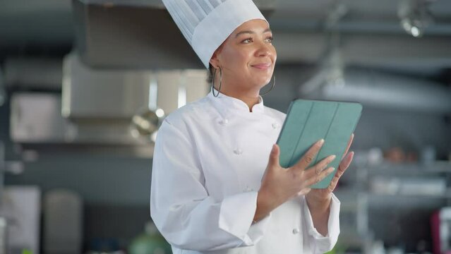 Restaurant Kitchen: Black Female Chef Cooking Delicious and Authentic Food, Uses Digital Tablet Computer. Professional Creates traditional Dish, using Healthy Ingredients for Recipe Preparation