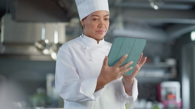 Restaurant Kitchen: Black Female Chef Cooking Delicious and Authentic Food, Uses Digital Tablet Computer. Professional Creates traditional Dish, using Healthy Ingredient, Prepare Meal Recipe. Medium