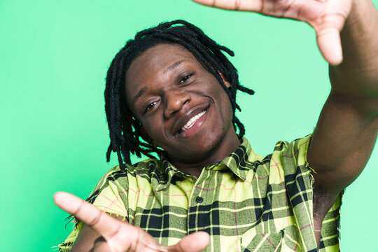 Young black man with dreadlocks smiling and making frame gesture