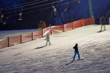 Ski drag lift in operation at night with lighting. Winter athletes on the slopes in the snow. Long...