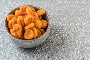 sweet dried apricots in a ceramic bowl on a grey plastic surface