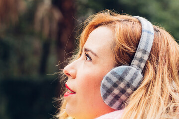 Side close-up of the face of a beautiful blonde woman, looking at the sky with an expression of hope and illusion, with space for purchase. earmuffs for the cold in winter.