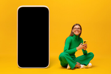 Young woman sitting on floor near huge phone mock up for app