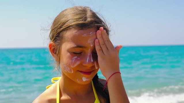 The child puts sunscreen on her face. Selective focus.