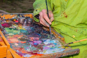 Cutout of an unrecognizable artist picking up a brush with paint on the color palette, selective...