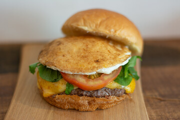 Cheeseburger with open bread, showing fried egg, tomato, arugula, cheese and patty.