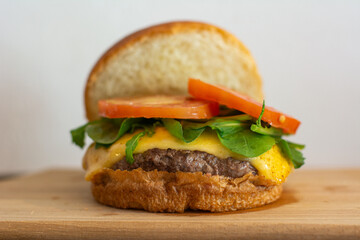 Cheeseburger with open bread, showing tomatoes, arugula, patty and cheese