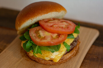 Cheeseburger with open bread, showing tomatoes, arugula, patty and cheese