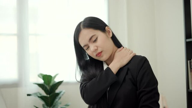 Office syndrome concept, Asian business woman works at computer, she experiences pain in neck and touches his neck with one hands, turns his head in attempt to relieve pain. 4k Resolution.