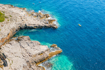 Top view of sportsmen or tourists kayaking in the turquoise transparent blue water of Adriatic sea rocky shore. Summer leisure activity in the canoe. 