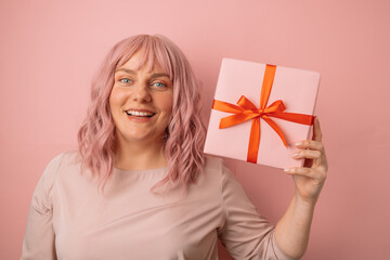 Happy young smile 30s woman showing gift box looking at camera isolated on pink background