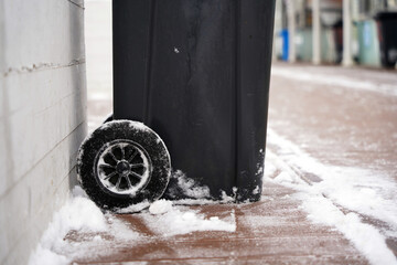 Black plastic garbage can with wheels on a snow-covered sidewalk