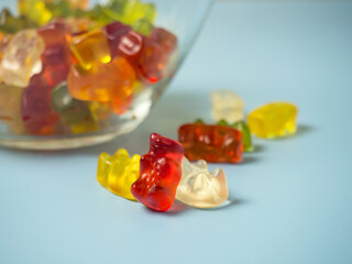 Bowl with tasty bright gummy bears on blue table