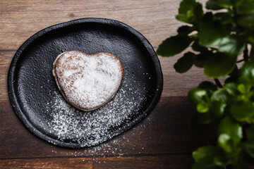 a heart-shaped donut on a plate, sprinkled with sugar, next to a plant