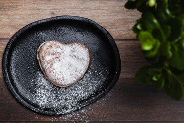 a heart-shaped donut on a plate, sprinkled with sugar, next to a plant