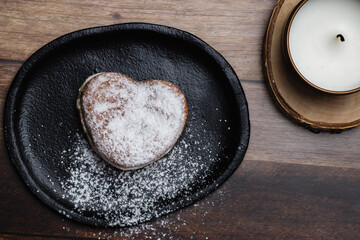 a heart-shaped donut on a plate sprinkled with sugar, next to a candle