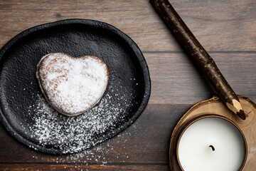 a heart-shaped donut on a plate sprinkled with sugar, next to a candle and a pencil