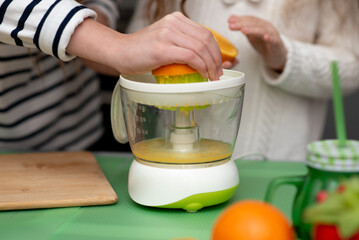 Two cute sister girls are making orange fresh juice.Hands close-up. They are in the kitchen at home. Family. Fresh fruit.
