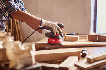 Female carpenter grinding wood with sandpaper in carpentry or diy workshop. Electric sander working...