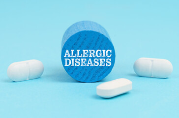 Pills lie on a blue surface, a wooden blue cylinder with the inscription - Allergic diseases