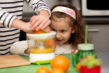 A little girl watches as orange juice is being prepared. Two cute sister girls are making orange fresh juice. They are in the kitchen at home. Family. Fresh fruit. Healthy eating.