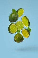 Creative idea with whole and sliced lime flying in the air isolated on bright blue background.