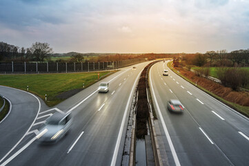 Driving cars on a highway with wet asphalt in Germany, sunset on a cloudy sky, motion blur, copy space, selected focus