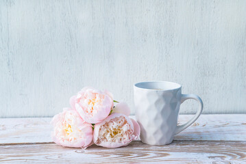 Celebration or holiday concept; white mug of coffee or tea and bouquet ofr pink roses on rustic white paint wooden background