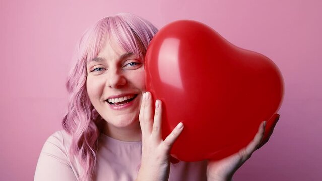 Valentine's day celebration. Young pretty caucasian glamour woman smiling holding red balloon shaped heart isolated on pink background.