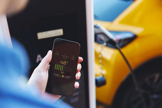 Man charging electric vehicle with cable looking at app on mobile phone
