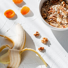 Delicious healthy muesli breakfast with oatmeal, chime, walnut and banana in a white bowl on a white table at sun lights in the morning. Vitamins food concept