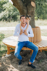 Fototapeta premium Dad and daughter sitting on a bench under a tree. Little girl in a black dress hugs dad. Spend time with family in the park. Father's Day