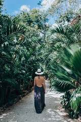 Girl in a luxury boutique hotel. Woman in sundress and hat walking in tropical jungle