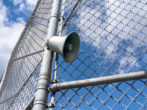 Low Angle View Of An Announcer Speaker Attached To A Fence At A Ball Park On A Bright, Sunny Day