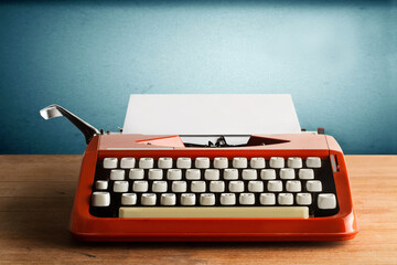 Máquina de escribir retro naranja de los años 60/70 sobre una mesa de madera rústica y un fondo azul. Vista de frente. Copy space