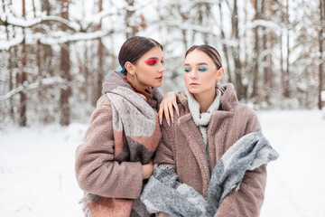 Two glamorous young girls models in fashionable clothes with a fur coat, sweater and vintage scarf in nature with snow