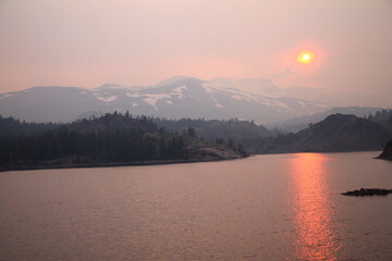 The sun reflecting on the lake through the fog and the ash of a wildfire in Yosemite National Park