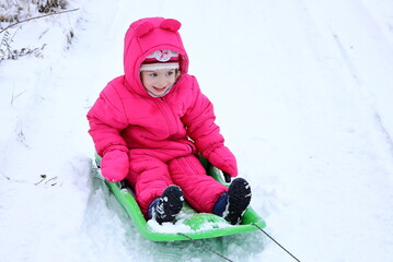 Happy little child enjoying the time on sled. A little girl rides a bobsleigh. Activity for winter...