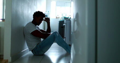 African man sitting on kitchen floor feeling desperate and despair