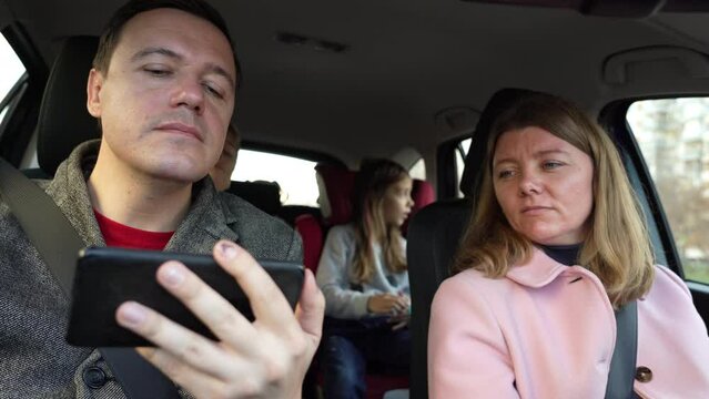 Girl driver drives car and man looks at camera on phone and discusses his appearance, overweight and touches his chin while trying to get through to interlocutor. Married couple with children on trip