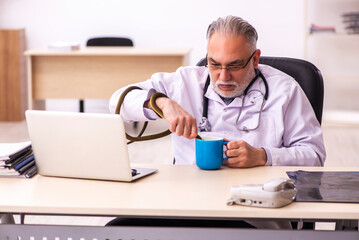 Obraz na płótnie Canvas Aged male doctor holding snake in the clinic