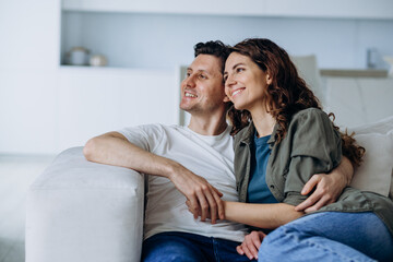 Happy newlyweds with dark hair sit on comfortable sofa in living room and discuss plans for future smiling broadly closeup