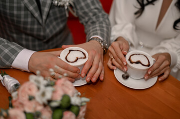 a man and a woman on a date in a cafe are holding cups of latte coffee. . a bouquet of flowers in the foreground.
