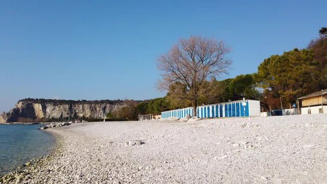 Rocky Castelreggio beach at Sistiana bay near Trieste in a winter sunny morning, with the Duino Castle and cliffs in the background
